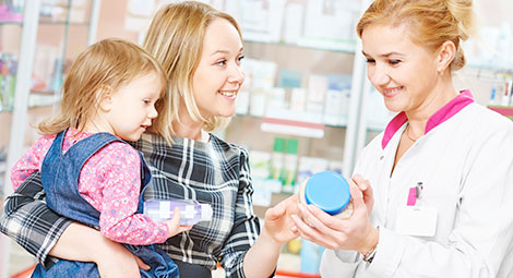 Pharmacist showing a mother a product whilst she holds her young child